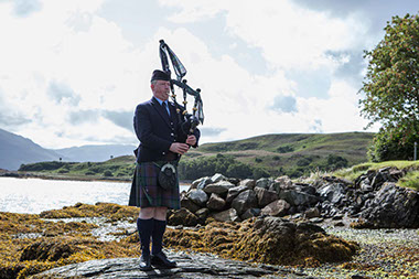 The Skye Piper playing by the shoreline on Skye